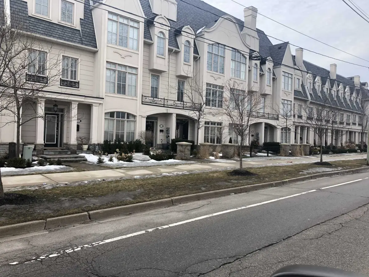 Row of townhouses with light stucco walls, white window surrounds and dark mansard roofs along a street