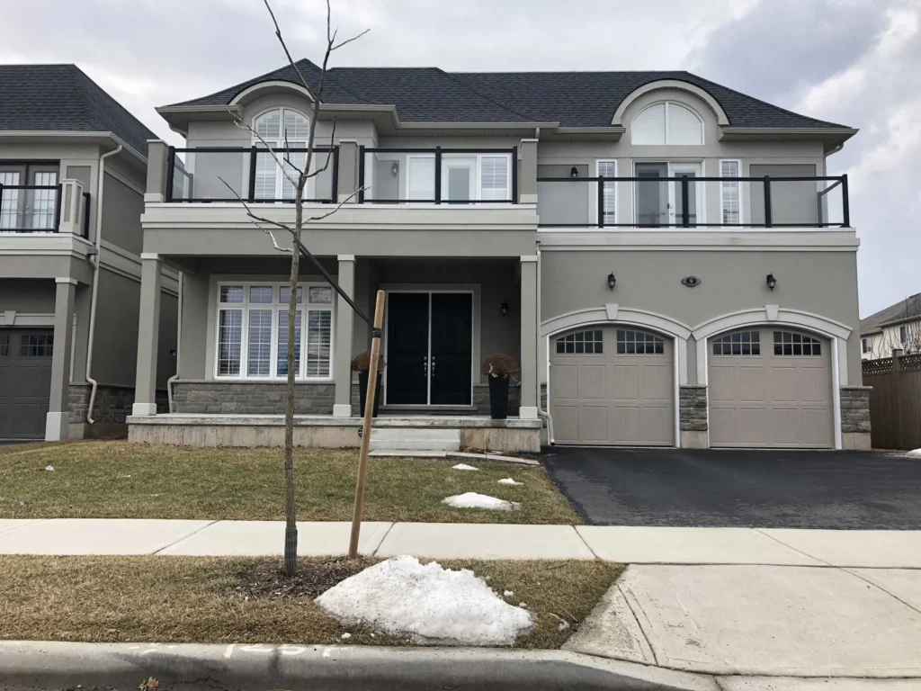 Grey stucco house with arched surrounds and keystones over two garage doors and a light band between the floors