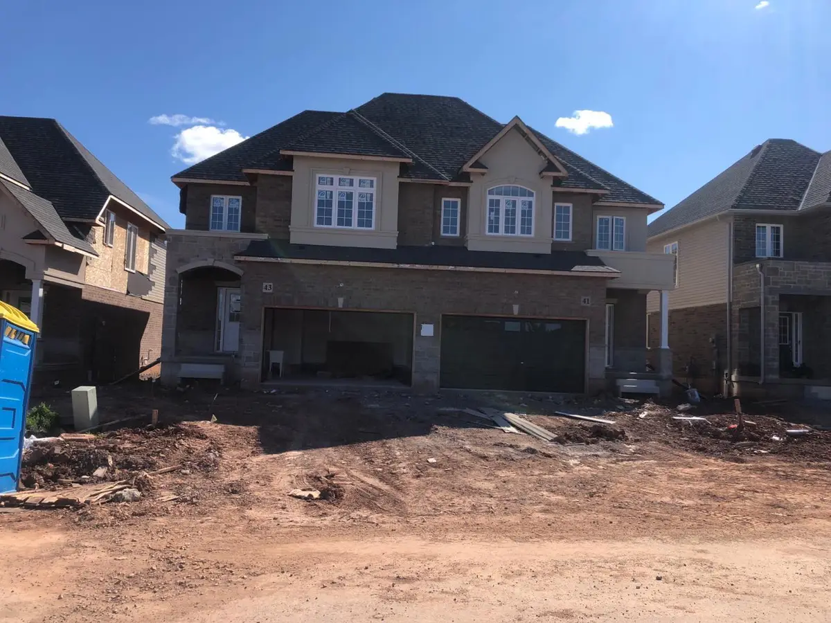 New semi-detached pair, numbers 41 and 43, with brick walls, light stucco on the second-floor bays and gable, stone around the arched entry and garage piers, and an ungraded dirt lot in front
