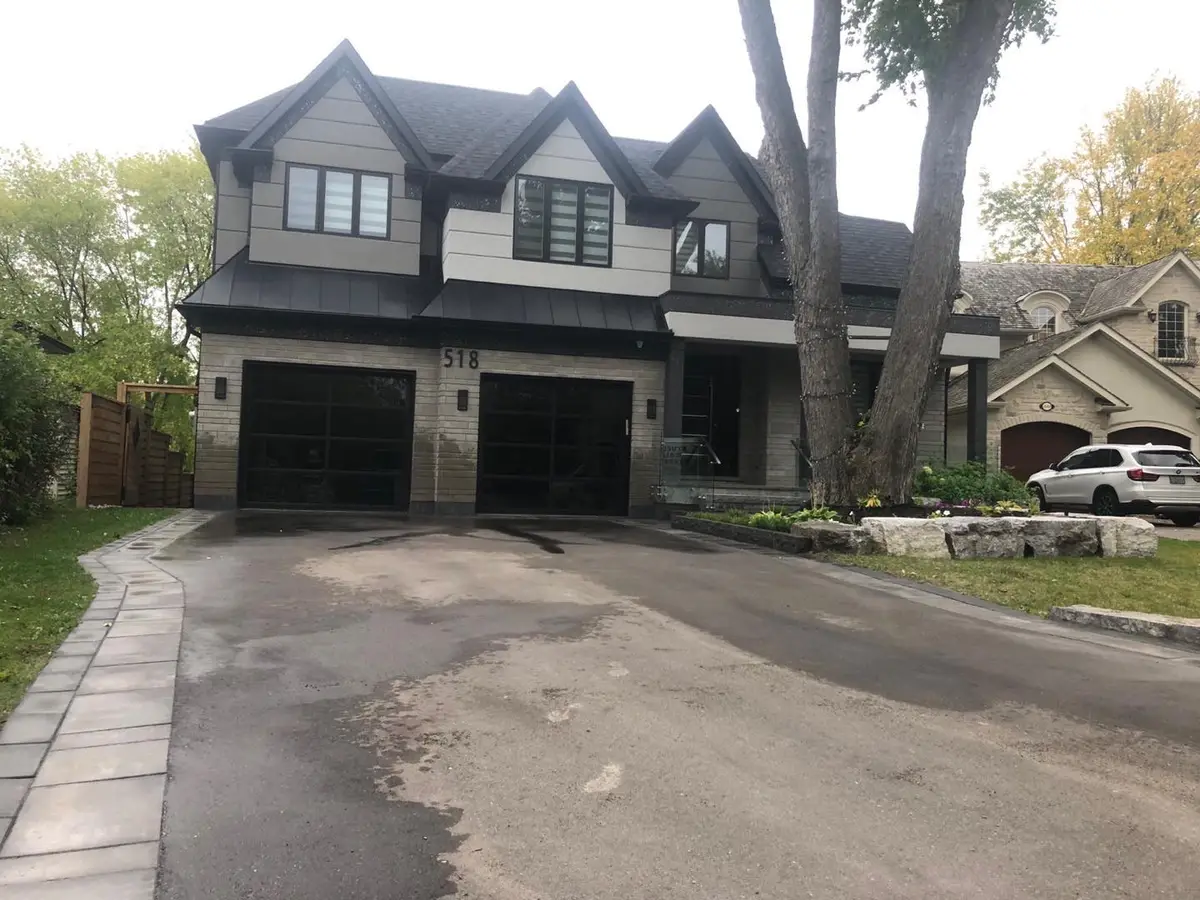 Two-storey house with grey and white wall panels, a stone base and two black garage doors behind a paved driveway