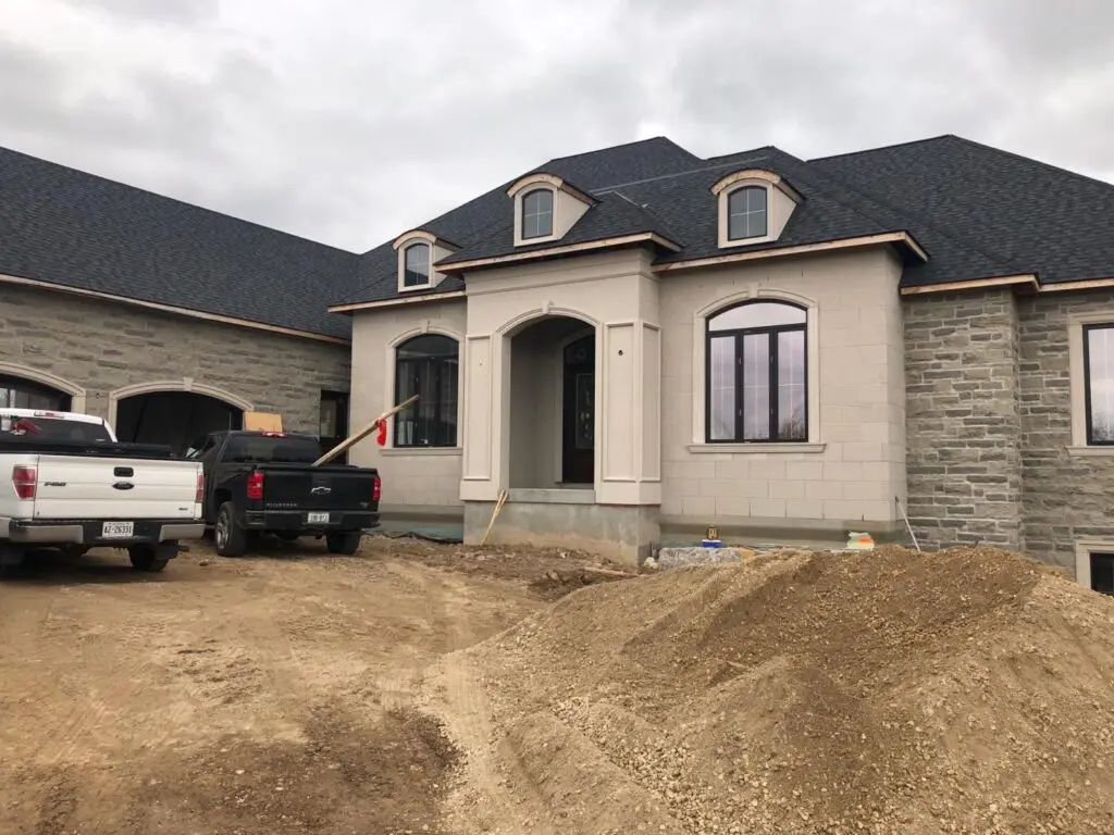 Light stucco house with an arched entrance and stone side walls, two pickup trucks parked in front
