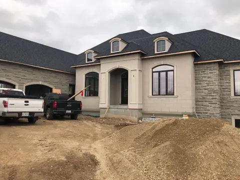 Bungalow with light stucco around arched windows and stone wings, two pickup trucks in the driveway