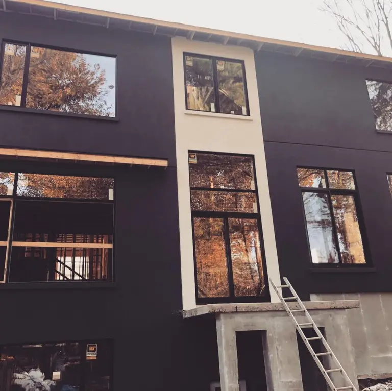 Three-storey wall with a black finish, a light vertical band around stacked windows and a ladder at the entrance