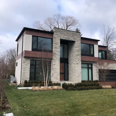 Modern two-storey house with white stucco panels, wood-tone bands and a tall stone entrance behind a lawn