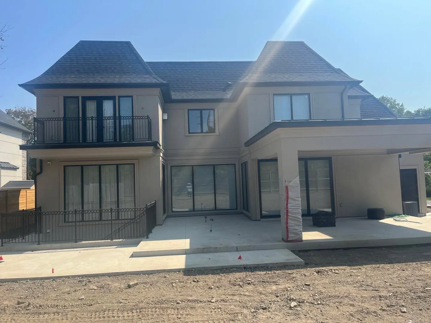 Two-storey house with beige stucco walls and a balcony on a lot with bare soil