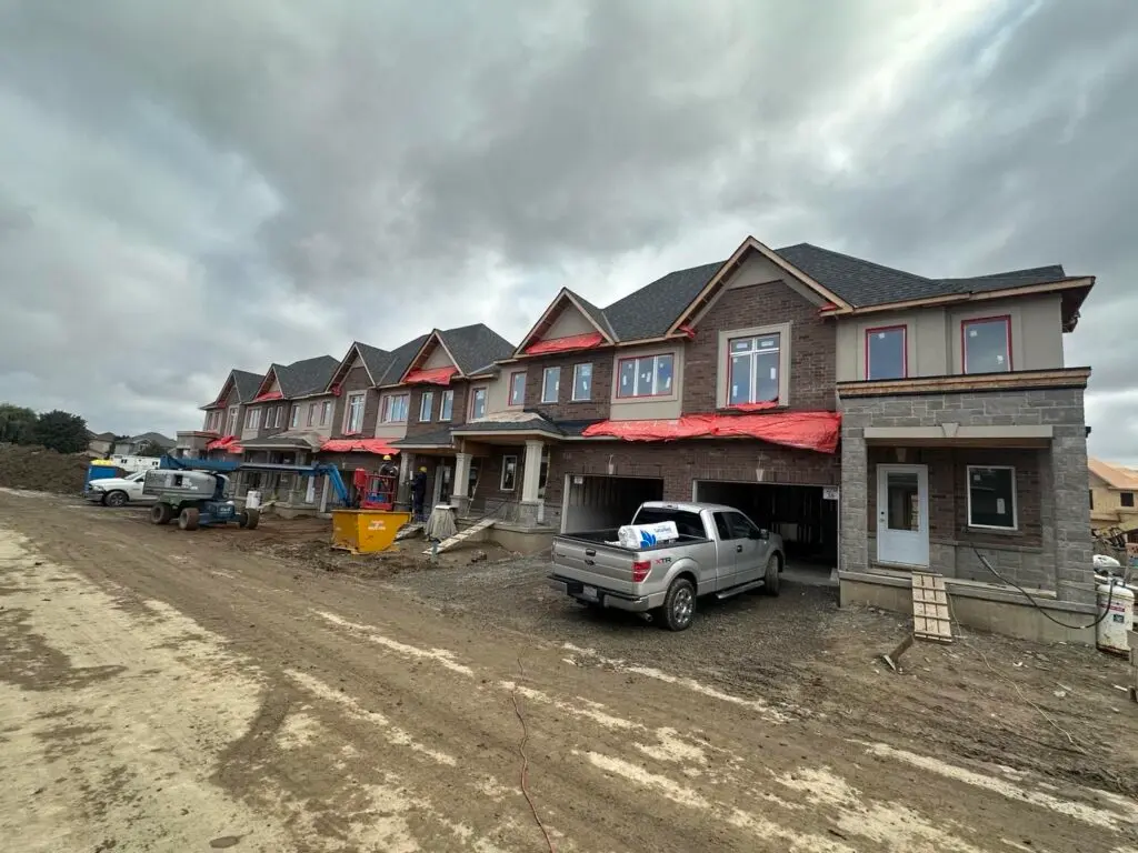 Row of new townhouses along a muddy site road, a pickup truck parked in front