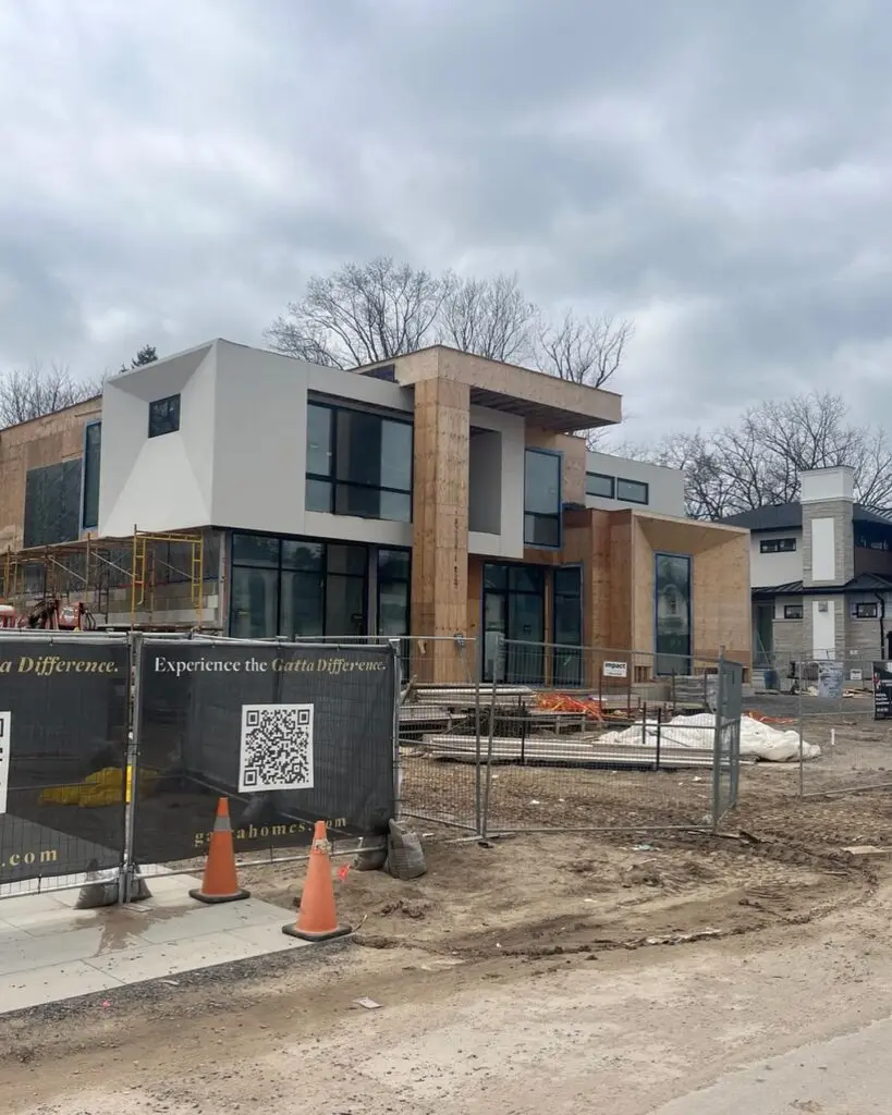 Modern house mid-construction with bare plywood sheathing on the entry column and lower walls beside finished light-grey panels above