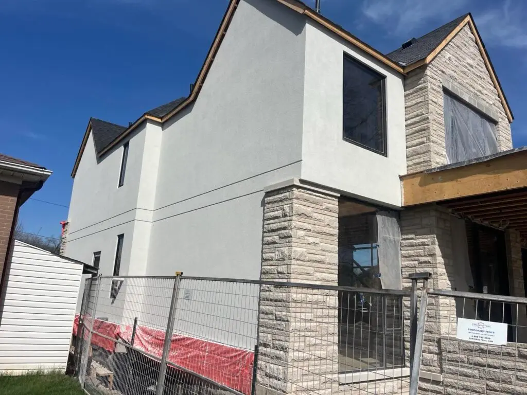Two-storey house with a light grey smooth stucco finish and a stone corner