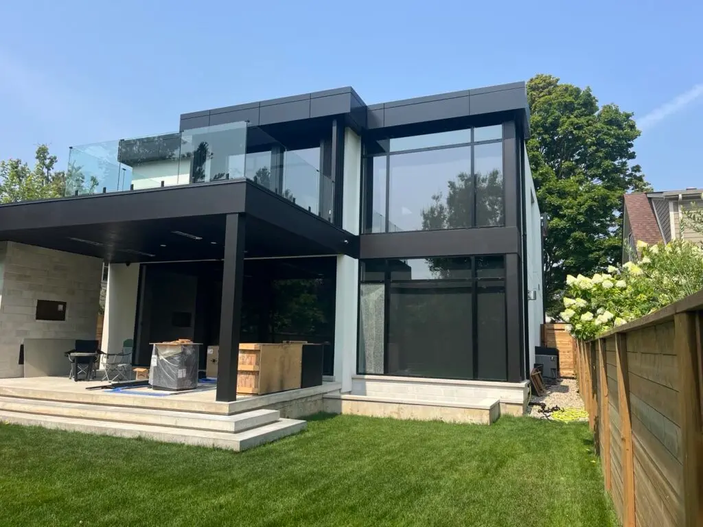 Modern two-storey house with white stucco walls, black upper panels, large black-framed windows and a glass balcony railing