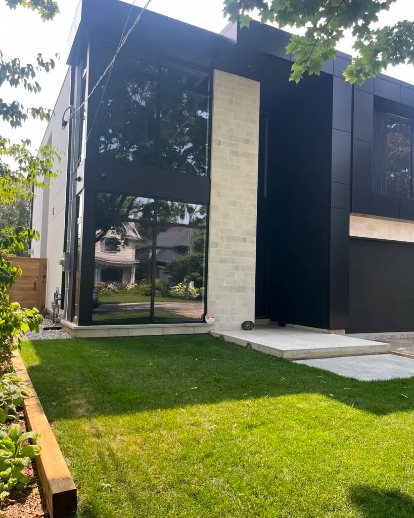 Modern house with dark walls and a light stone column beside the entrance, lawn in front