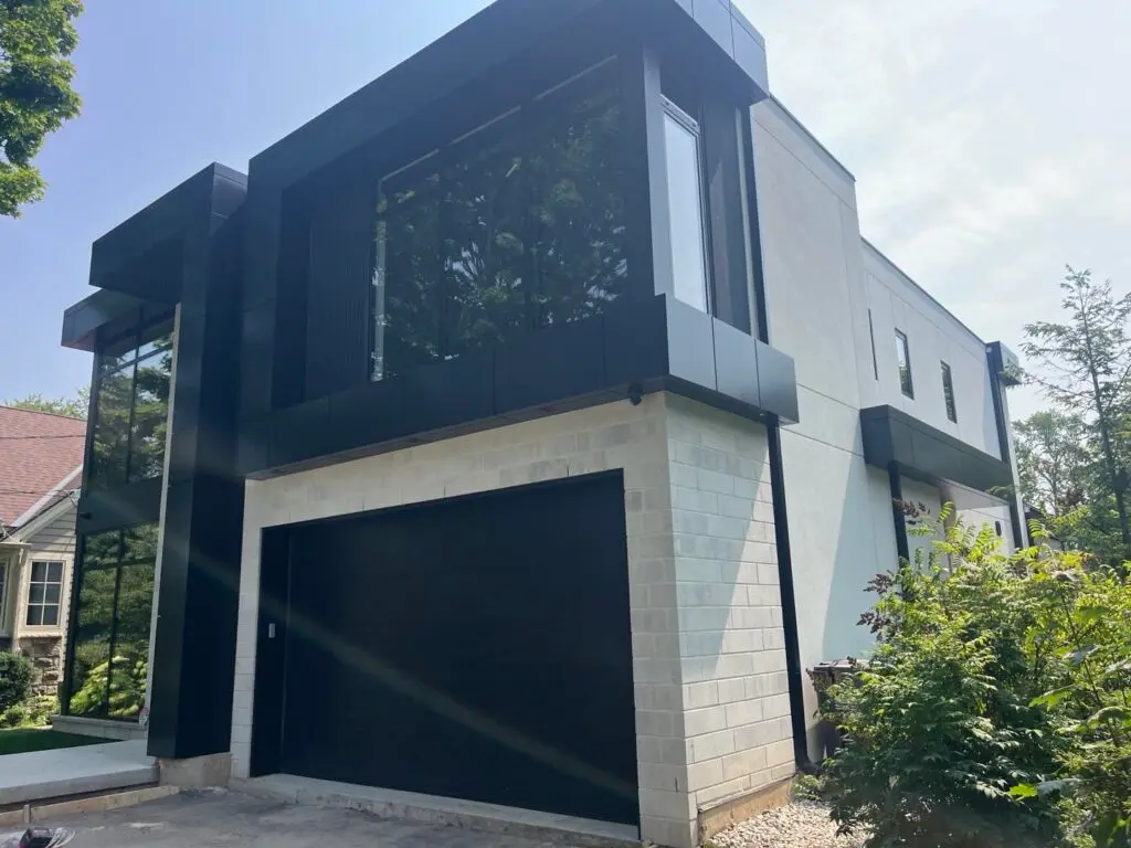 Modern house with white stucco walls, black panel cladding and a black garage door
