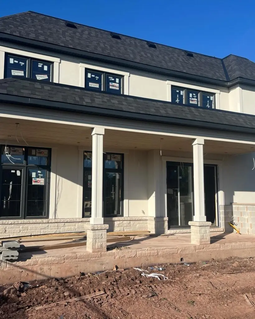 Front porch with square columns and new windows still carrying their stickers, bare soil in front