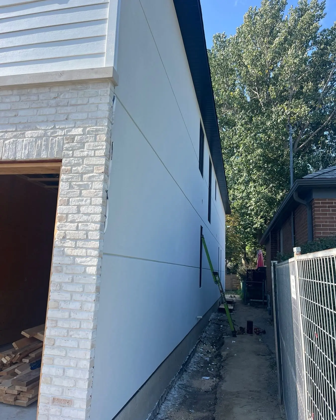 Long white stucco side wall meeting bare soil in a narrow side yard beside a wire fence