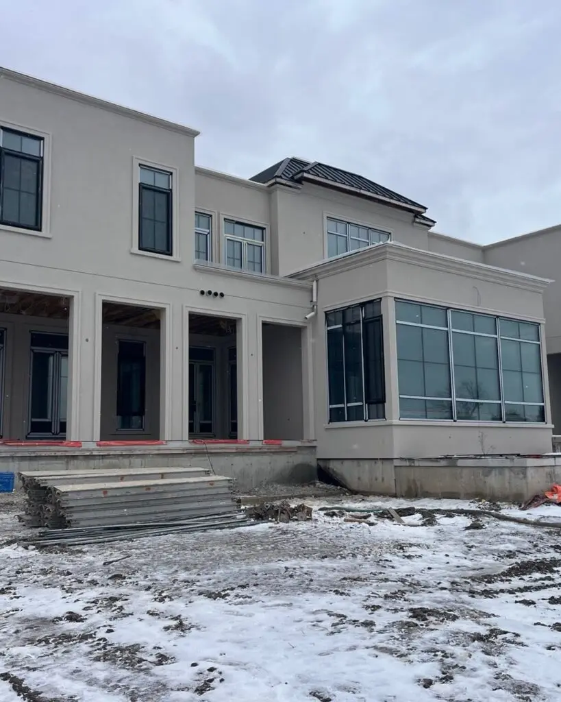Large light-coloured building with square columns and a glass corner room, snow on the bare lot